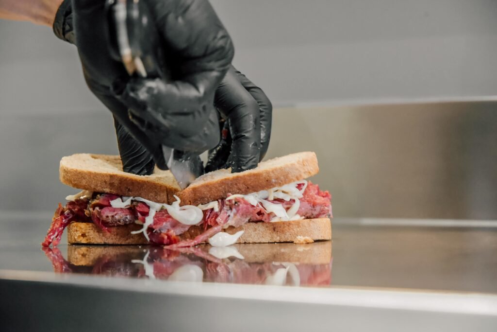 pexels-photo-15146531-15146531 Close-up of a chef's hands in gloves carefully cutting a meat sandwich.