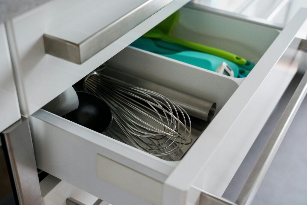 pexels-photo-3722563-3722563 Open kitchen drawer showcasing organized utensils including a whisk and scoop.