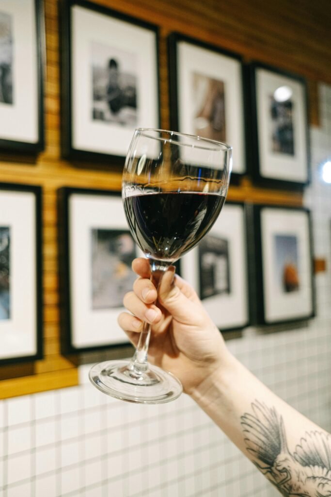 pexels-photo-4491289-4491289 Hand holding a glass of red wine in an art gallery setting with blurred background.