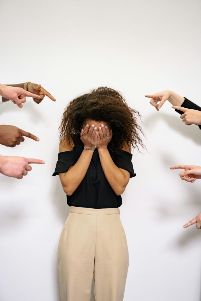 pexels-photo-7640730-7640730 A stressed woman covers her face as multiple hands point accusatorily in a studio setting.
